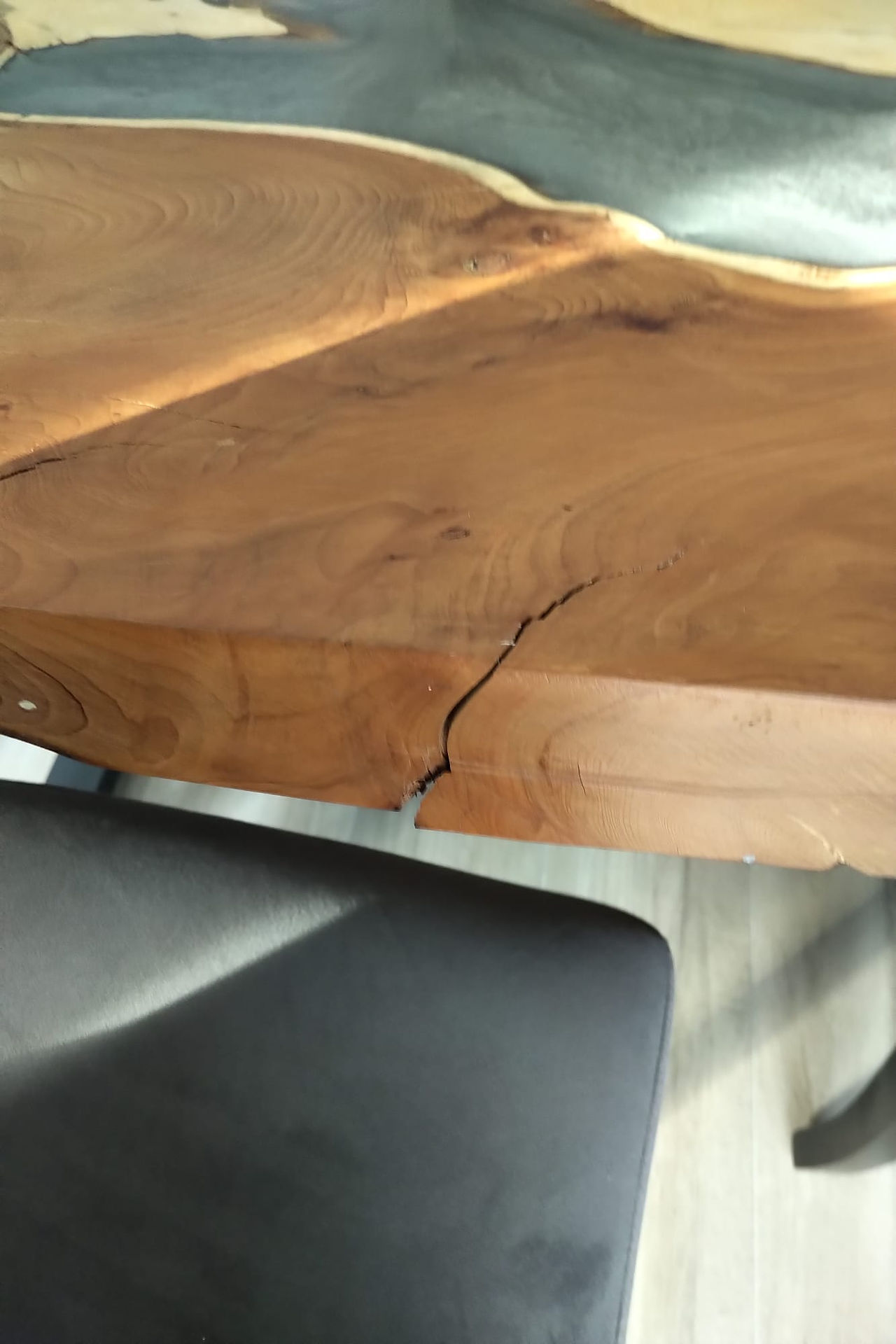 A wooden table with a gray resin top sits in a modern kitchen. The table has metal legs and visible woodworking joints.