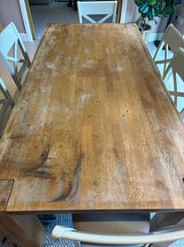 A rectangular wooden dining table with visible watermarks, scratches, and faded color. The table appears to be in need of repair and refinishing.