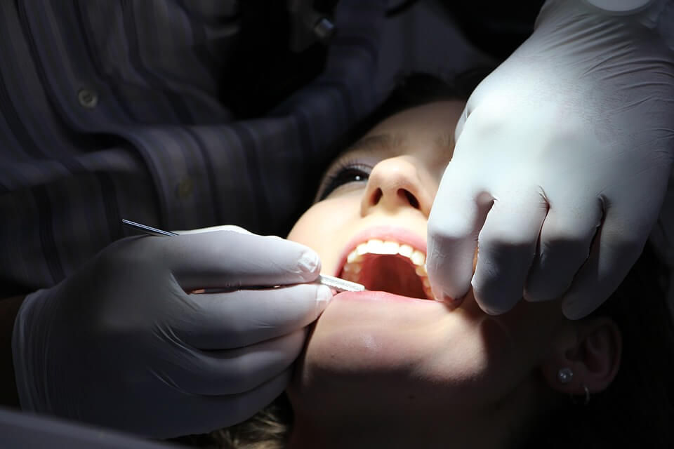 A dentist's gloved hands hold open a patient's mouth during an examination.