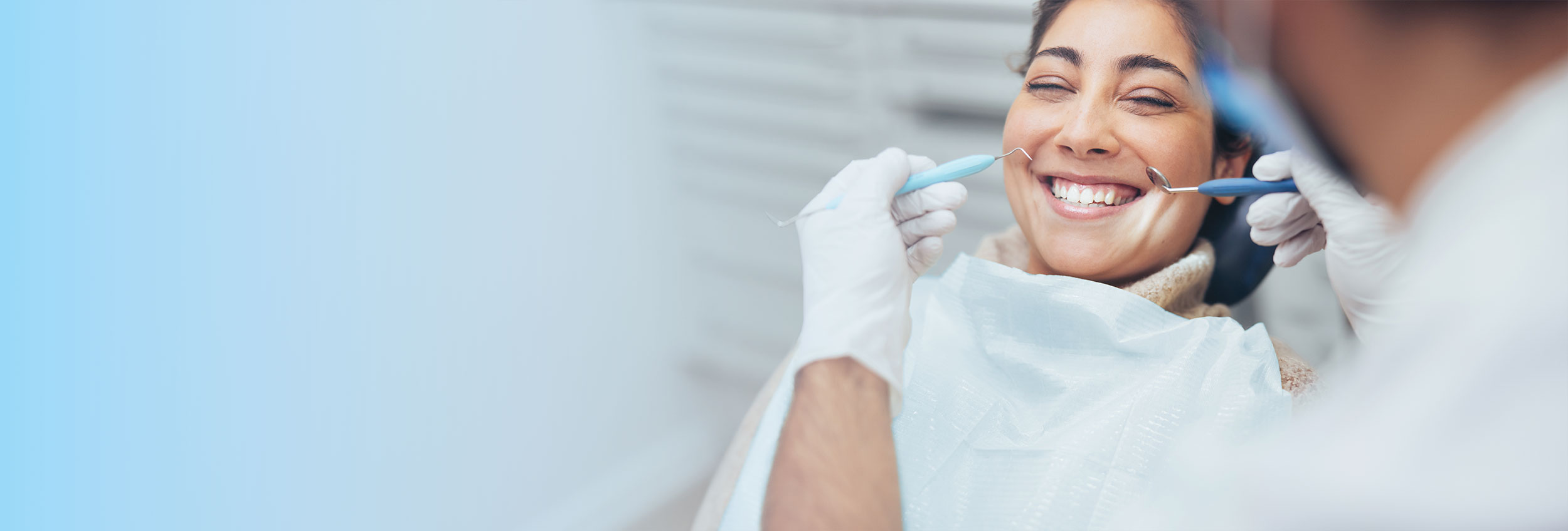 Woman smiling during a dental examination while a dentist holds dental tools