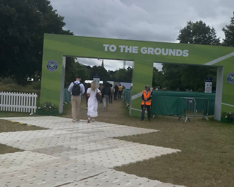 People walking under a green entrance at Wimbledon that says "To The Grounds"