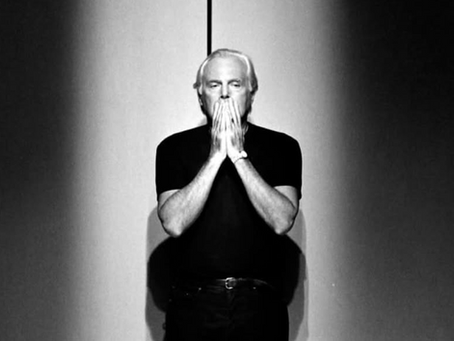 A black and white photo of Giorgio Armani holding his hands over his mouth
