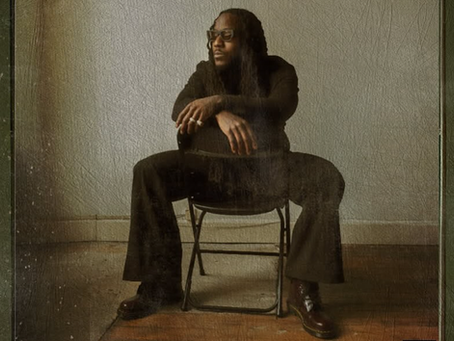 Ace Hood sits in a chair with his hands crossed over the back of it