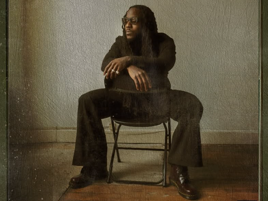 Ace Hood sits in a chair with his hands crossed over the back of it