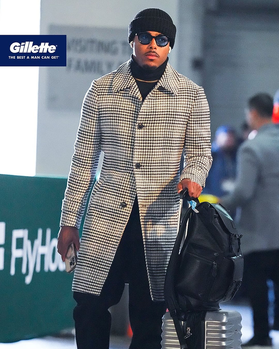 Marcus Jones walking in a tunnel wearing a black and white houndstooth overcoat with black trousers and a black beanie