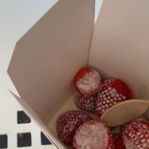 A white paper box with strawberries and cream inside