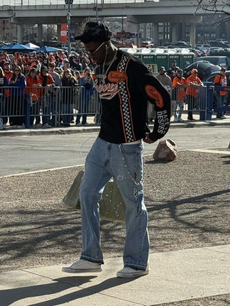 An NFL player walking on a sidewalk wearing a black and orange sweater with a checkerboard stripe and jeans