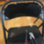 Black folding chair with back rest partially removed on wooden floor,. Screwdriver and pliers on seat, suggesting repair in progress.