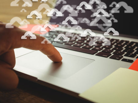 Close-up of a finger pressing a laptop touchpad with cloud upload icons overlaying the image