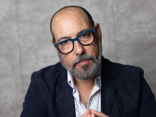 Confident sales leader in blazer and glasses seated against neutral background