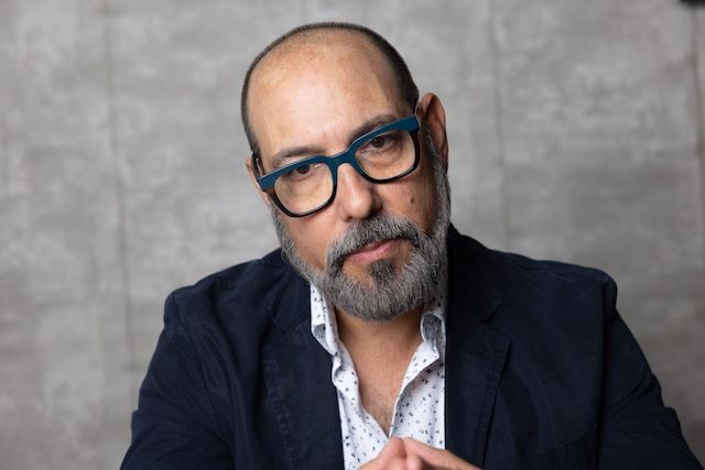 Confident sales leader in blazer and glasses seated against neutral background
