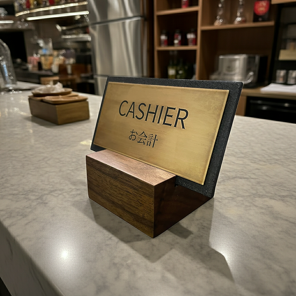 重厚なウォールナットの木製台座に、ビンテージ加工が施された真鍮プレートを差し込んだ、和モダンな卓上レジサイン。真鍮プレートにはエッチング加工で、英語の「CASHIER」と日本語の「お会計」が視認性高く刻まれています。インダストリアルな質感が際立つ接写