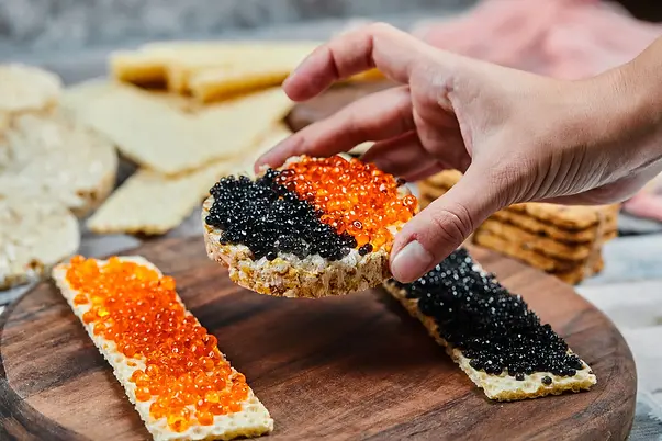 taking-cracker-sandwich-with-red-black-caviar-scaled.webp