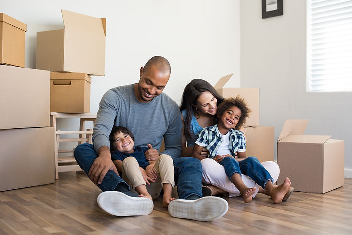 Two adults and one child smiling, surrounded by stacked moving boxes.