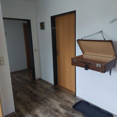 Offener brauner Koffer hängt an Kette an der Decke eines Raumes mit Holztüren und Holzfussboden
