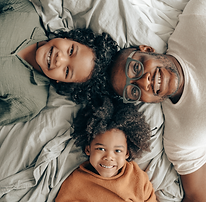 Father and children lying on bed smiling and looking up.