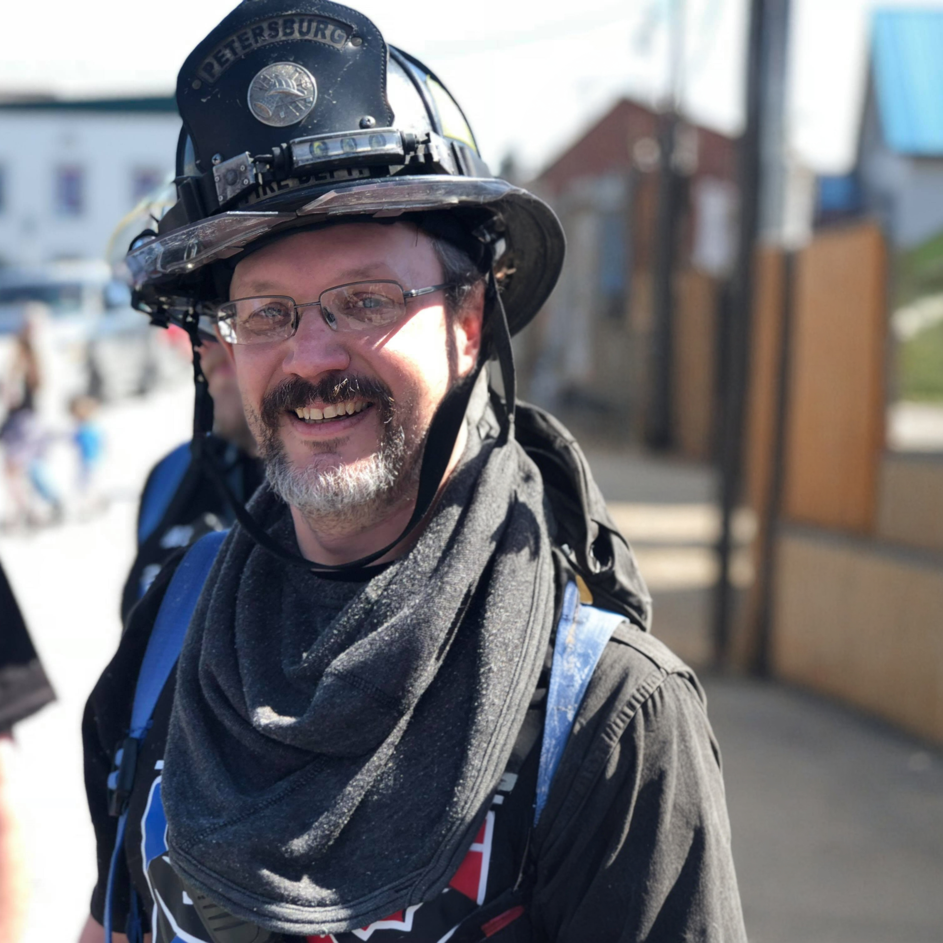 Smiling firefighter wearing glasses and black helmet during daylight, cheerful expression.