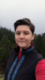 Person in vest smiles for photo, trees in background on a cloudy day.