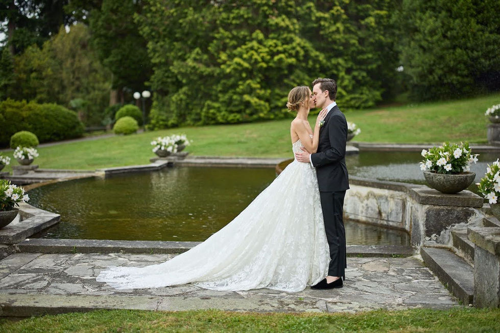 Bride and groom kissing by a tiered stone fountain with the lush villa gardens in the background.