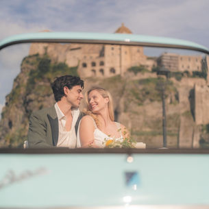 The couple in the pale-blue vintage car with Castello Aragonese in the background
