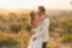 A couple embraces and kisses in a scenic, sunlit landscape with greenery. The mood is romantic, with warm tones at sunset.