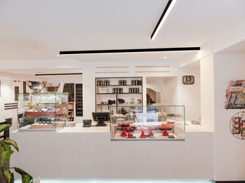 Kuchentheke, weiß mit kubischen Glasvitrinen, Kuchensortiment, Weinsortiment, schwarze gerade Leuchtkörper