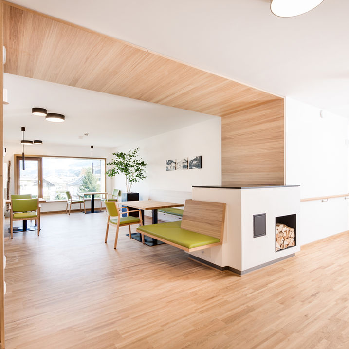 aufenthaltsbereich mit offenem kamin, ofenbank mit grünem Bezug, Wandelement aus holz, fenster mit ausblick dorf