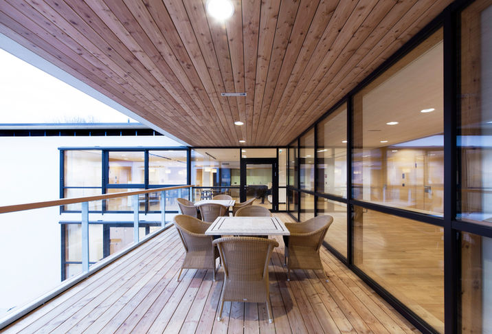 loggia mit holzverkleidetem boden und decke, glasbrüstung links, vollverglaste fassade rechts, tischgruppe und korbstühle