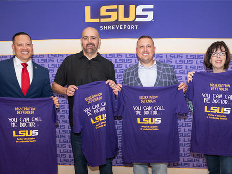 Four LSUS graduates hold up t-shirts recognizing successfully defended dissartations.