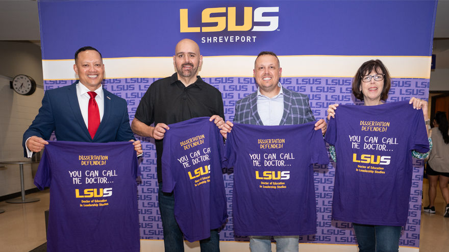 Four LSUS graduates hold up t-shirts recognizing successfully defended dissartations.