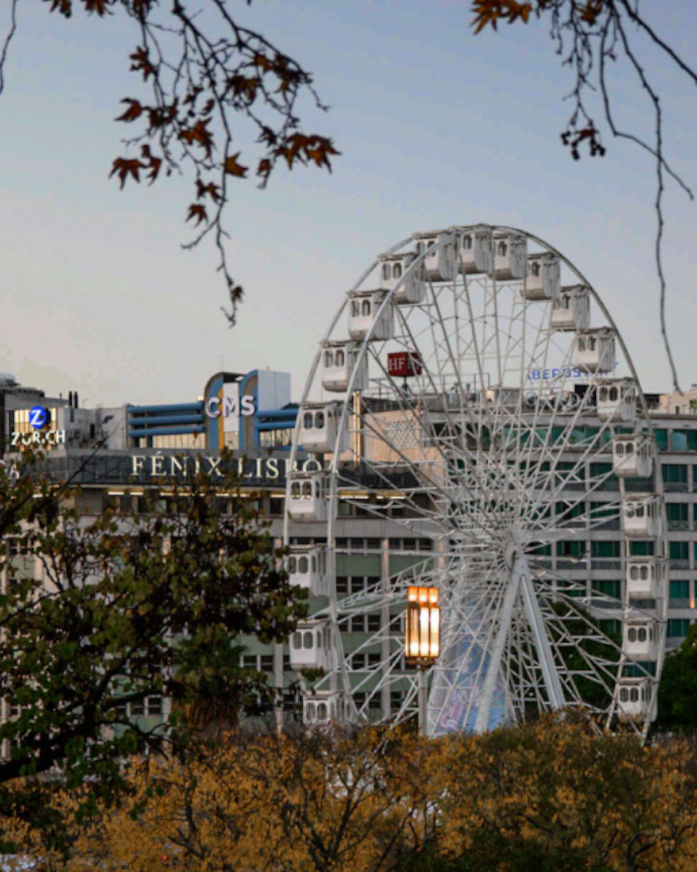 A colorful Ferris wheel against a dusky sky in Parque Eduardo VII, Lisbon, Portugal.