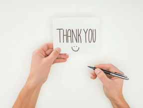 hands writing THANK YOU :) on note