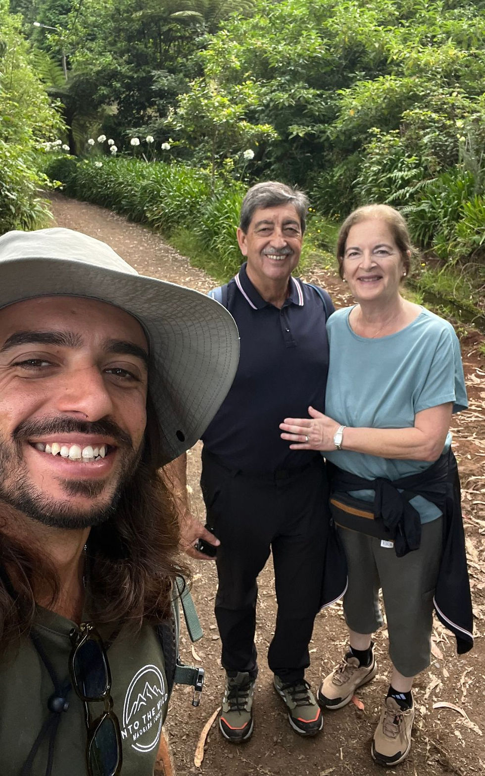 Smiling selfie of three hikers on a leafy garden trail; one wears an Into the Wild shirt.