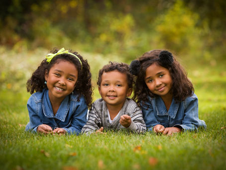 Three smiling young children on the grass.