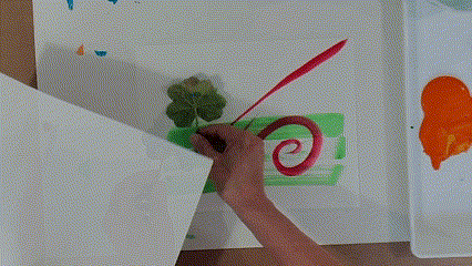 An artist covers up a portion of a painted pattern with a piece of paper; when they lift the paper, it is revealed that they stamped in a new blue paint shape.