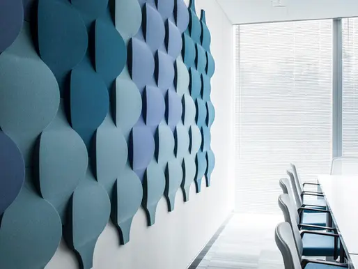 Modern conference room with a textured blue wall design, white table, and chairs. Sunlight filters through blinds, creating a calm atmosphere.