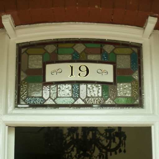 Hand painted gold leaf and black restored house number on stained glass window above front door.