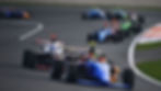Race cars on track, with a blue car numbered 22 leading. Fast-paced action, vibrant colors, and a curving road in the background.