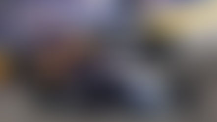 Racing cars on track with vibrant red, yellow, and purple designs. Car number 5 leads. Blue and yellow barriers line the course. Energetic mood.