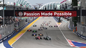 Race cars speed on a track under a banner reading "Passion Made Possible" in Singapore. Excited crowds and colorful urban backdrop.