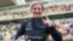 Smiling Doriane Pin in a black suit holds up one finger in celebration. Logos on suit include Mercedes, Pirelli. Stadium background.