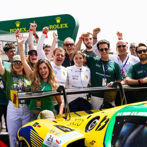 Cheering team and fans pose beside a yellow-green race car at a Rolex track, arms raised in celebration.