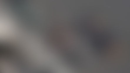 Three Formula 1 cars race closely on the track. The cars are silver, black with green, and blue with logos. The mood is competitive.