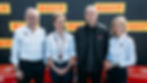 Four people smiling in front of a Pirelli backdrop. Three wear white shirts, one in a black jacket. Red podium numbers partially visible.