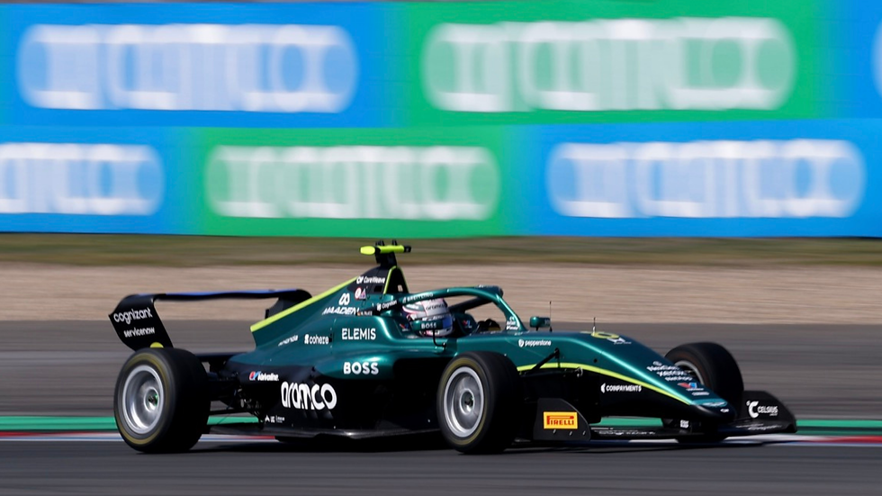 Green and black race car speeds on track, blurred background with blue-green banners, visible logos on car, dynamic action, sunny day.