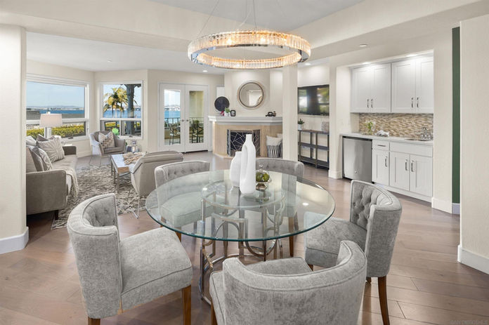 Dining Room at 1st St, Unit 117, Coronado - glass dining table top with chrome base, rounded light gray chairs, with a round chrome chandelier 