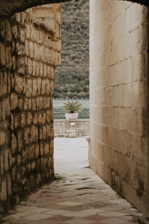 Ancient stone passage opening toward calm water and a potted palm