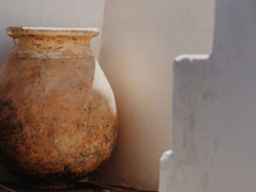 Weathered clay vessel beside white walls in warm sunlight