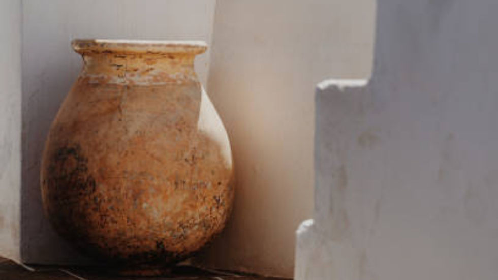 Weathered clay vessel beside white walls in warm sunlight