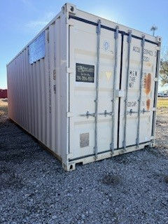 White shipping container on a gravel lot outdoors, with faded black markings and a bright blue sky overhead.